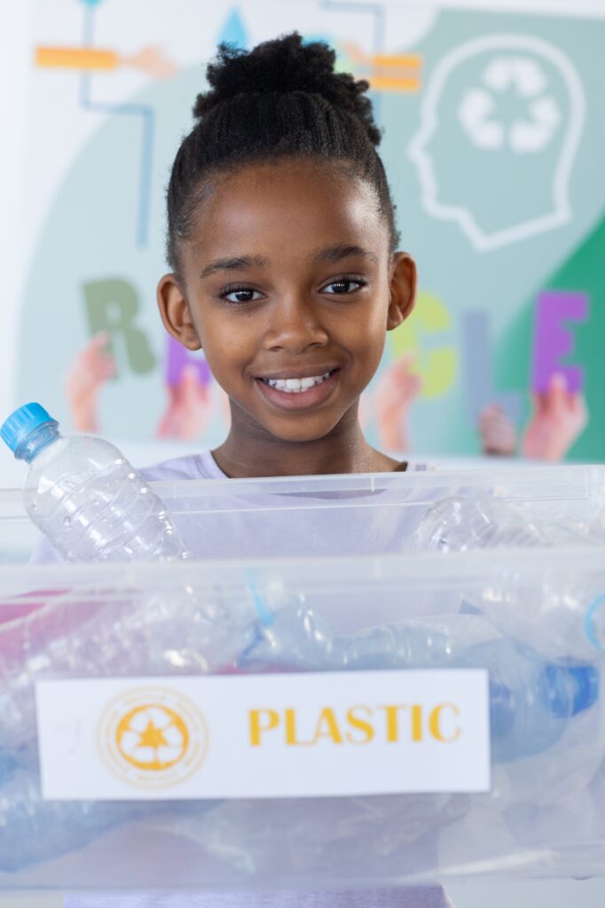 Recycling plastic bottles, african american girl smiling and holding container in school classroom